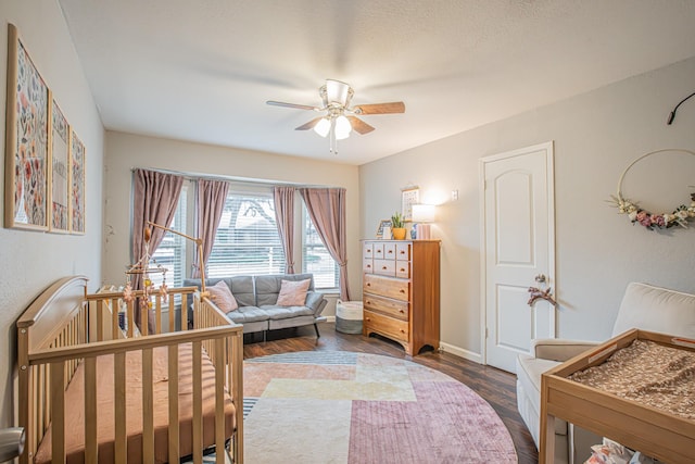 bedroom featuring a crib, dark hardwood / wood-style floors, and ceiling fan