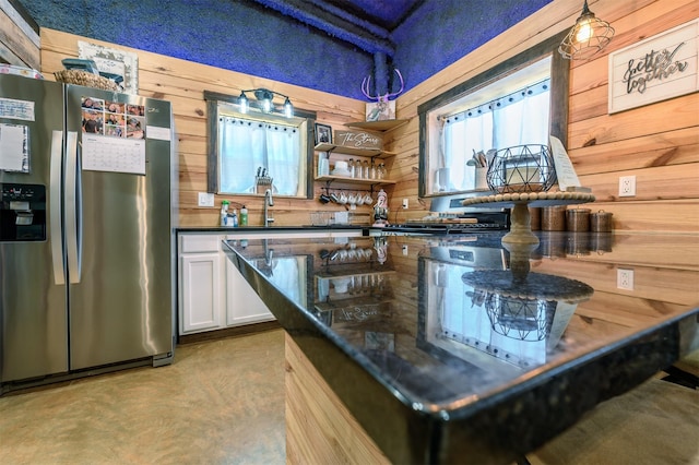 kitchen featuring white cabinetry, sink, wood walls, and stainless steel fridge with ice dispenser