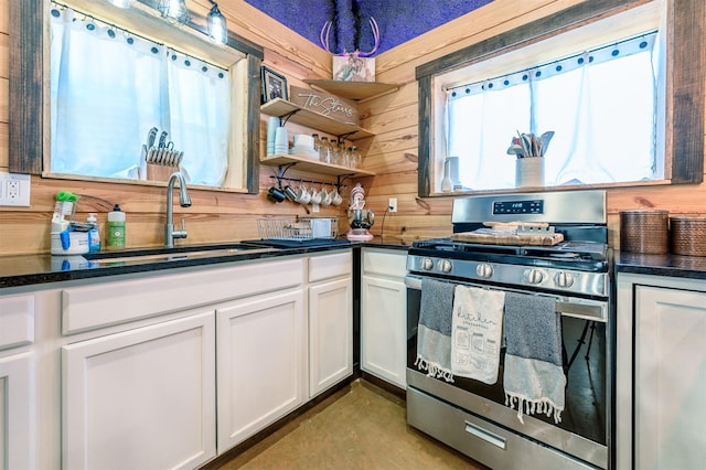 kitchen with sink, stainless steel gas range, white cabinets, and wood walls