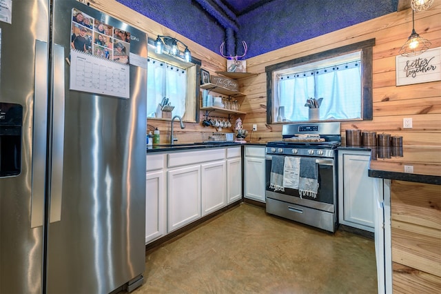 kitchen with appliances with stainless steel finishes, wood walls, white cabinetry, sink, and hanging light fixtures