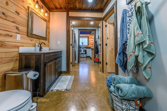 bathroom with wooden walls, concrete floors, vanity, toilet, and wooden ceiling