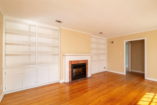 unfurnished living room with a tiled fireplace, crown molding, built in shelves, and light hardwood / wood-style flooring