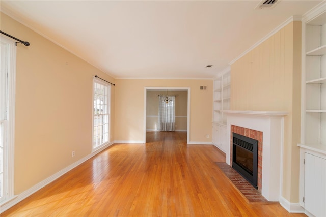 unfurnished living room with built in features, wood-type flooring, ornamental molding, a brick fireplace, and a chandelier