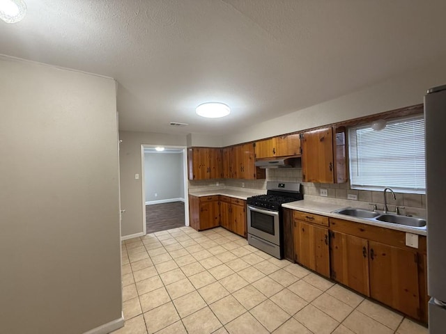 kitchen featuring sink, stainless steel gas range oven, a textured ceiling, light tile patterned floors, and backsplash