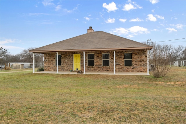 back of property with brick siding, a yard, a patio, a chimney, and a shingled roof