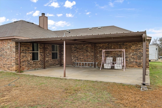 back of house featuring a yard, a patio, brick siding, and a chimney