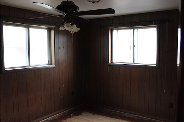 empty room with ceiling fan, wood-type flooring, and wooden walls