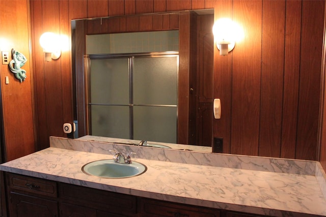 bathroom with vanity, wood walls, and a shower with shower door