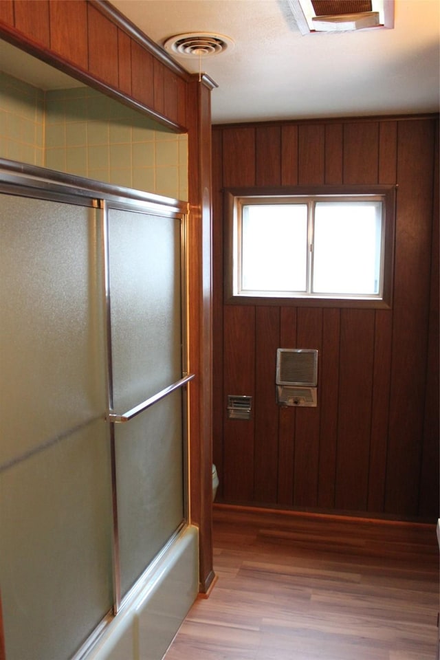 interior space featuring hardwood / wood-style flooring, bath / shower combo with glass door, toilet, and wood walls