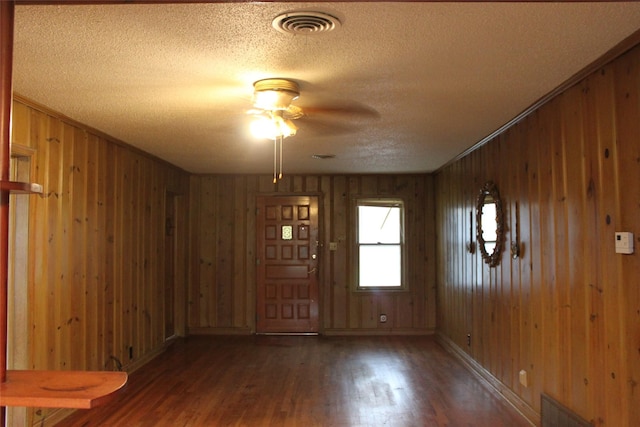 foyer featuring dark hardwood / wood-style floors, wood walls, ceiling fan, crown molding, and a textured ceiling