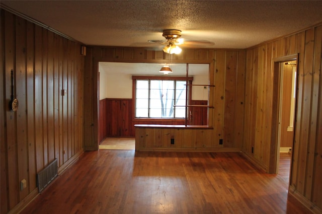 empty room with wood-type flooring, ceiling fan, a textured ceiling, and wood walls