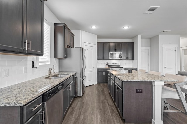 kitchen featuring sink, dark wood-type flooring, appliances with stainless steel finishes, a center island, and light stone countertops