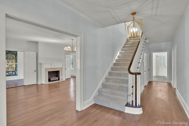 stairway with a fireplace, hardwood / wood-style floors, a textured ceiling, and a notable chandelier