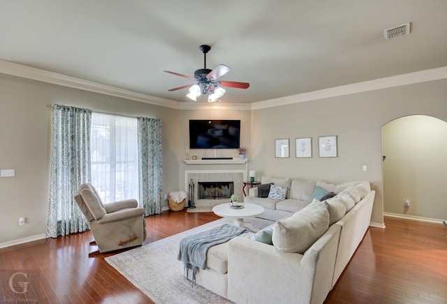 living room with ornamental molding, dark wood-type flooring, a tile fireplace, and ceiling fan