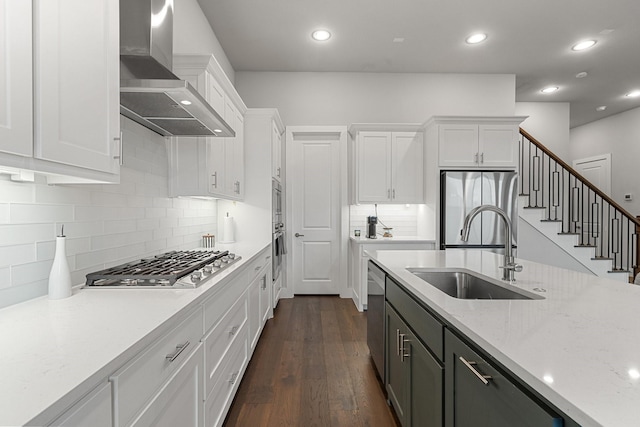 kitchen featuring appliances with stainless steel finishes, sink, white cabinets, light stone counters, and wall chimney exhaust hood