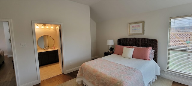 bedroom featuring ensuite bath, lofted ceiling, and hardwood / wood-style floors