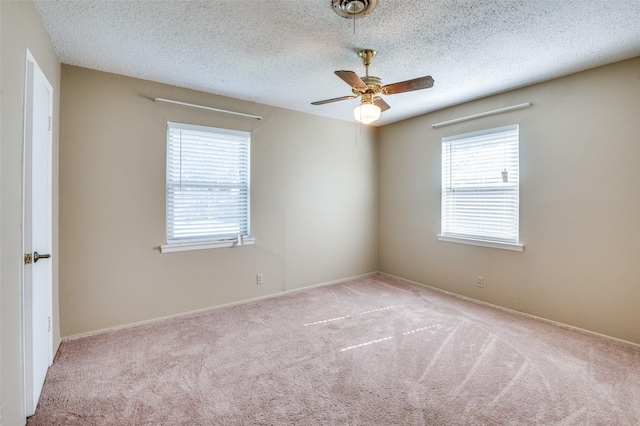 empty room with a wealth of natural light, light carpet, ceiling fan, and a textured ceiling