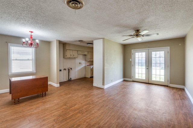 unfurnished living room with ceiling fan with notable chandelier, a textured ceiling, light wood-type flooring, and french doors