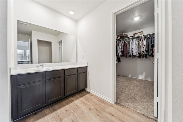 bathroom featuring a walk in closet, vanity, baseboards, wood finished floors, and visible vents
