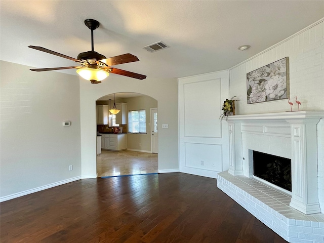 unfurnished living room featuring wood-type flooring, a brick fireplace, and ceiling fan