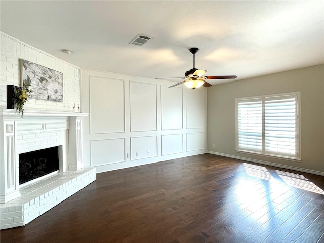 unfurnished living room featuring a brick fireplace, dark wood-type flooring, and ceiling fan