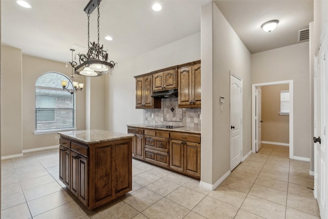 kitchen with hanging light fixtures, light tile patterned floors, black electric cooktop, a kitchen island, and backsplash