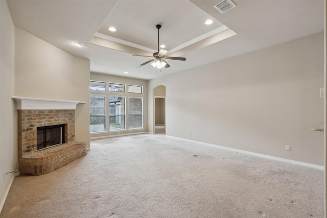 unfurnished living room featuring ceiling fan, carpet flooring, a tray ceiling, and a brick fireplace