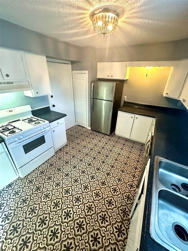 kitchen featuring under cabinet range hood, white cabinetry, white gas range oven, freestanding refrigerator, and dark countertops