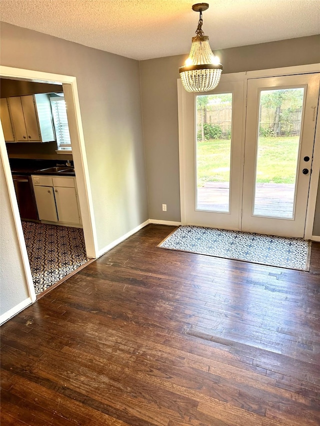 doorway to outside featuring dark wood-type flooring, a sink, a textured ceiling, and baseboards