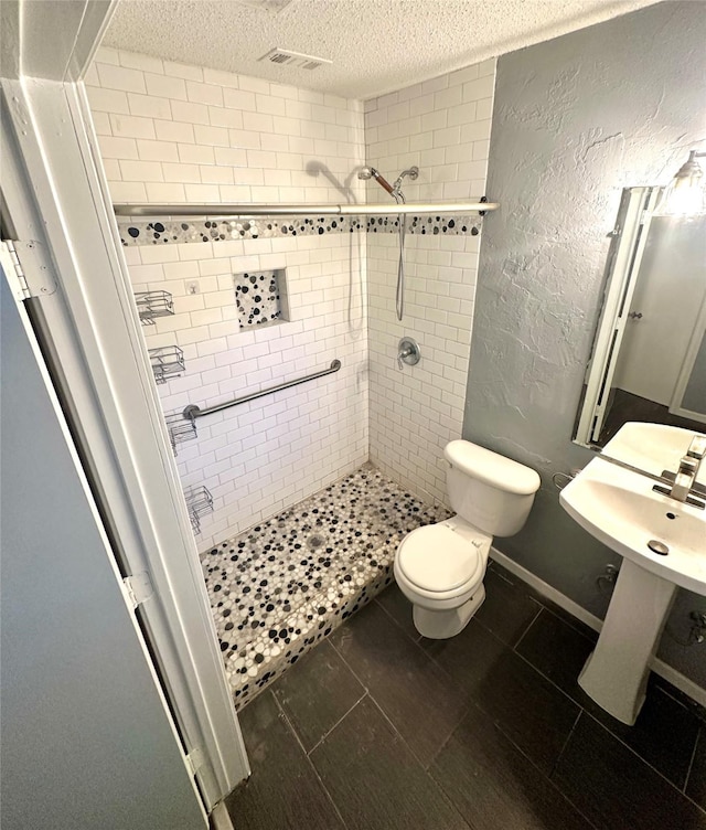 full bath featuring visible vents, a textured wall, toilet, a textured ceiling, and a shower stall