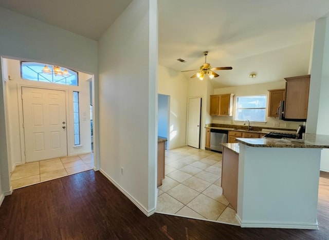 kitchen featuring sink, vaulted ceiling, dark stone counters, kitchen peninsula, and stainless steel appliances