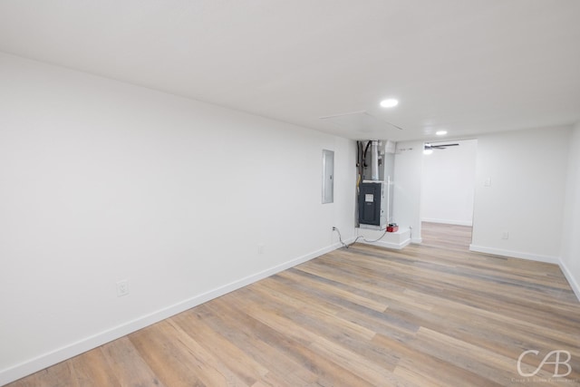 basement featuring heating unit, electric panel, and light wood-type flooring