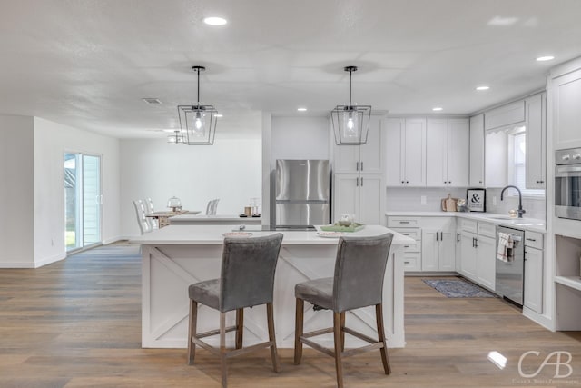 kitchen with a kitchen island, appliances with stainless steel finishes, hanging light fixtures, and white cabinets