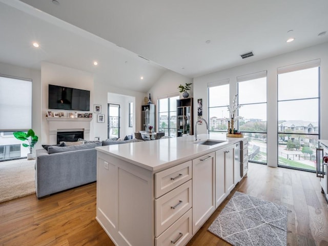 kitchen with sink, light hardwood / wood-style floors, white cabinets, and a center island with sink