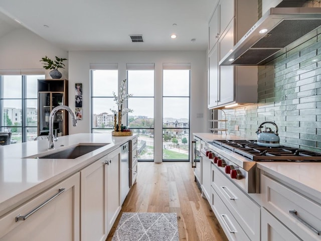 kitchen with range hood, stainless steel gas stovetop, white cabinetry, sink, and light wood-type flooring