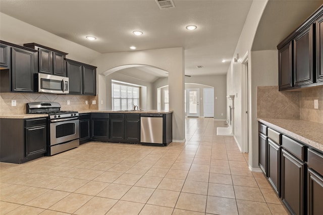 kitchen with tasteful backsplash, light tile patterned floors, vaulted ceiling, and stainless steel appliances