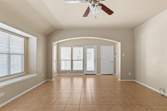 empty room featuring light tile patterned flooring, vaulted ceiling, a wealth of natural light, and ceiling fan