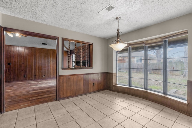 unfurnished dining area with wooden walls, a textured ceiling, and light tile patterned floors