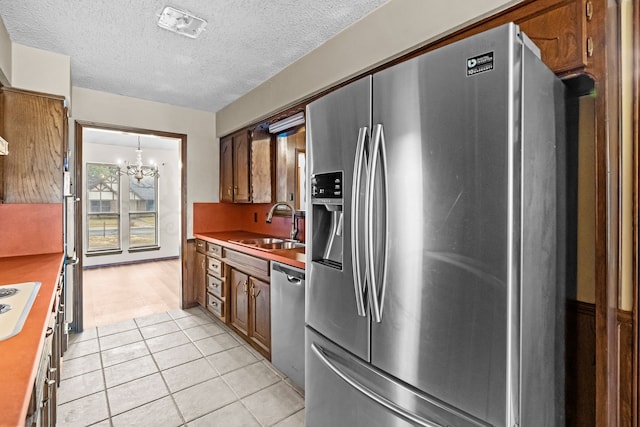 kitchen featuring appliances with stainless steel finishes, sink, a chandelier, light tile patterned floors, and a textured ceiling