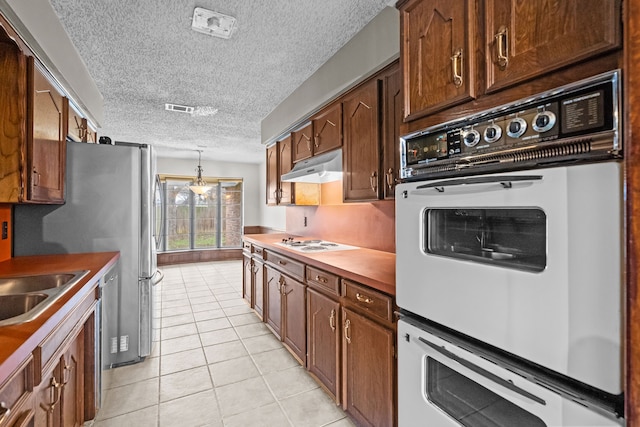 kitchen featuring sink, a textured ceiling, light tile patterned floors, pendant lighting, and white appliances