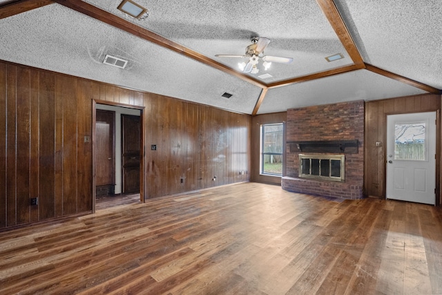 unfurnished living room with hardwood / wood-style floors, wooden walls, a fireplace, lofted ceiling, and ceiling fan