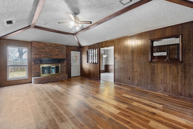 unfurnished living room featuring a brick fireplace, wooden walls, hardwood / wood-style floors, and a textured ceiling