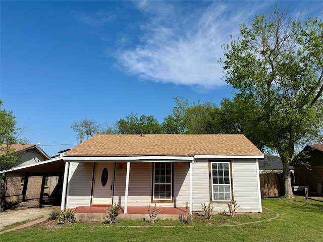 ranch-style home featuring fence, a carport, a front lawn, a porch, and a shingled roof