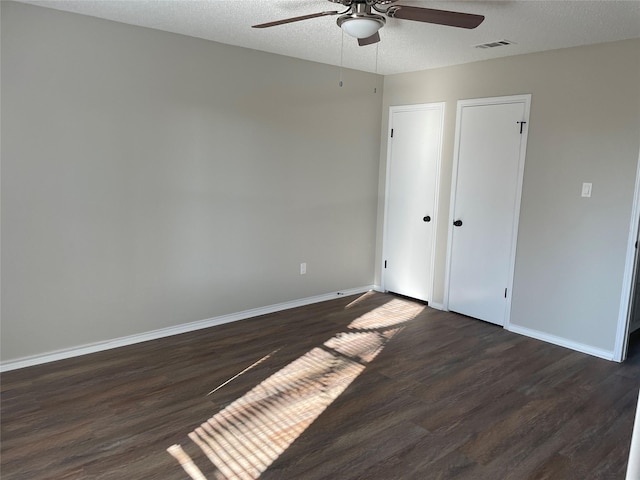 empty room with ceiling fan, dark wood-type flooring, and a textured ceiling