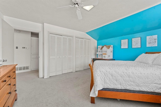 carpeted bedroom with ceiling fan, a textured ceiling, vaulted ceiling, and multiple closets