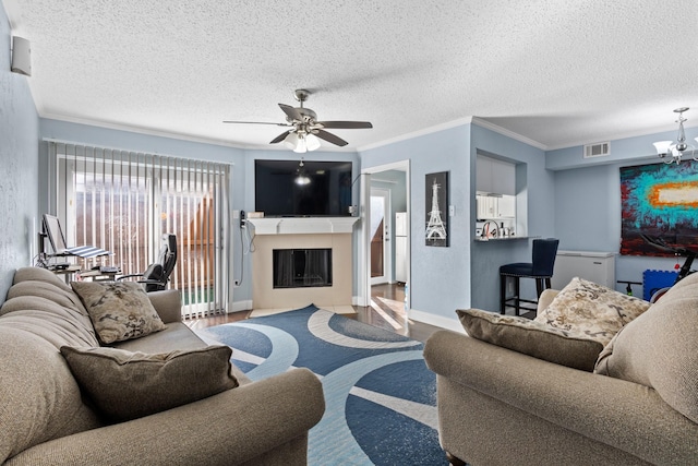 living room with crown molding, visible vents, a fireplace with flush hearth, wood finished floors, and ceiling fan with notable chandelier