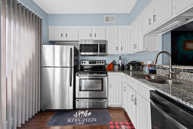 kitchen with stainless steel appliances, sink, white cabinets, and dark stone counters