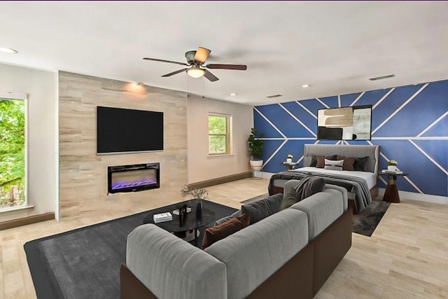 living room with a tiled fireplace, ceiling fan, and light hardwood / wood-style floors