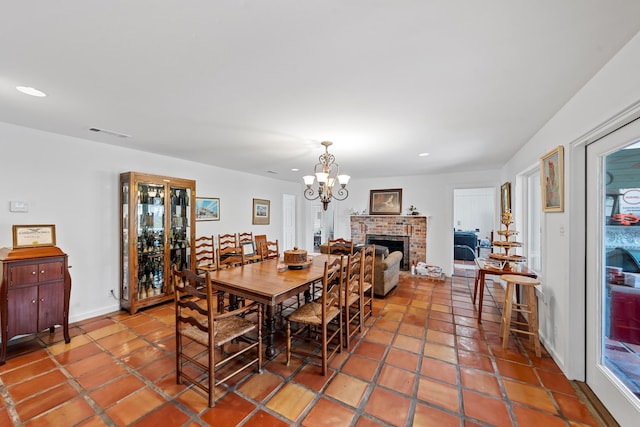 dining space with a chandelier, tile patterned flooring, and a brick fireplace