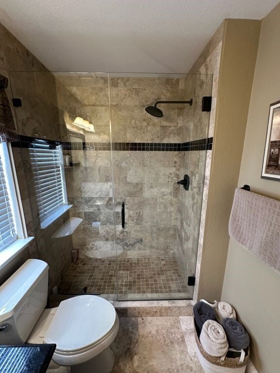 bathroom with a textured ceiling, a shower with door, and toilet